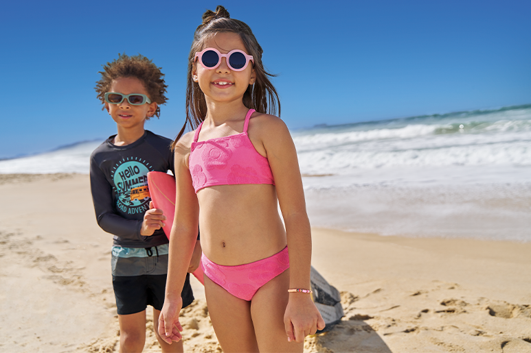 Crianças na praia usando roupas com proteção UV.