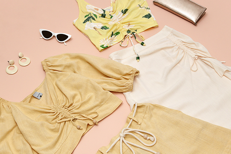 Brincos, blusa cropped e saia dourada, óculos, blusa cropped estampada, saia branca e bolsa em fundo rosa.