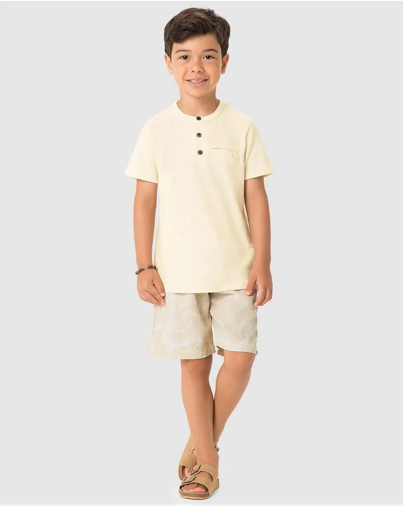 Menino veste um conjunto da marca Carinhoso, com camiseta com gola de botões e bermuda na cor off white. 