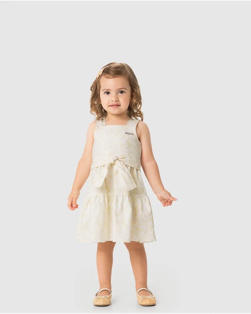 Criança menina veste um vestido off white com laço frontal para batizado, da marca Carinhoso.
