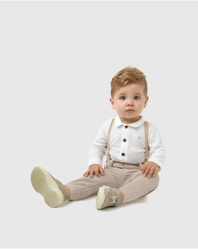 Bebê veste conjunto com calça de suspensório e body de manga longa com gola polo e botões. Marca Carinhoso.