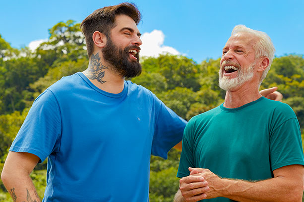 Pai e filho conversam e dão risada. Eles vestem camisetas básicas da Malwee.
