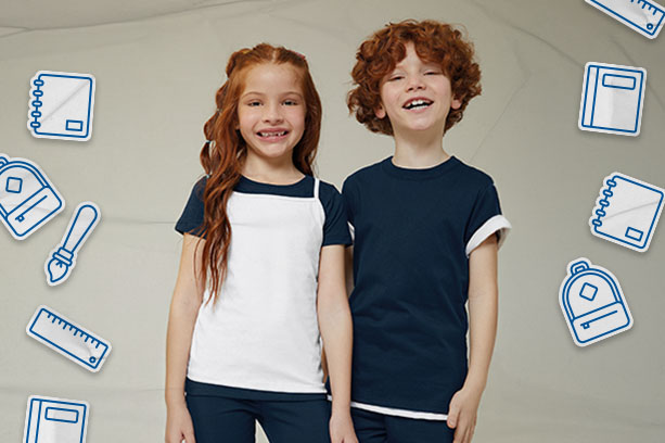 Volta às aulas: Um menino e uma menina, ambos ruivos, vestem roupas básicas da Malwee Kids em tons de branco e azul-marinho. O fundo neutro está decorado com desenhos de materiais escolares: réguas, mochilas, cadernos.