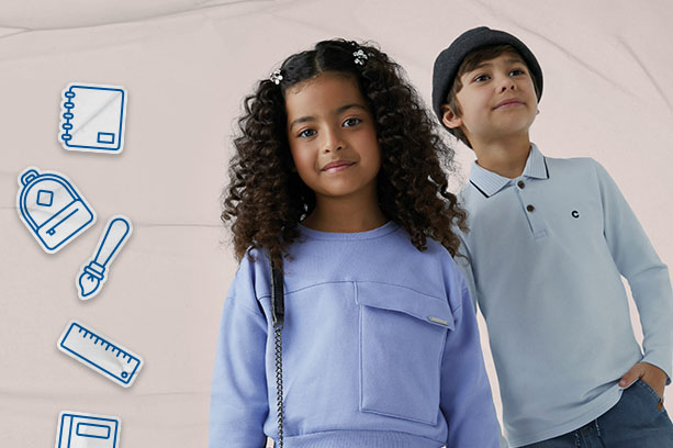 Volta às aulas: Duas crianças sorridentes vestem peças da marca de moda infantil Carinhoso para ir à escola. A menina é negra de cabelos cacheados presos em lacinhos, e veste um moletom azul claro. O menino é branco e veste um gorro cinza e uma camisa polo azul clara de manga comprida. O fundo é bege, com desenhos de materiais escolares.