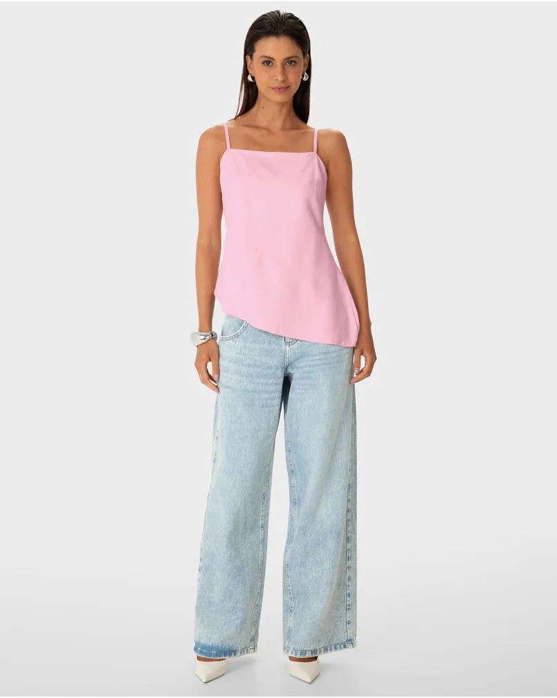 Modelo morena da marca Enfim, de cabelos molhados, veste uma regata com barra assimétrica, mais comprida do lado esquerdo, com calça jeans clara wide leg.