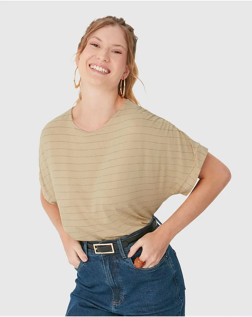 Modelo branca sorridente com cabelos presos veste uma camiseta listrada na cor bege e shorts jeans escuros da marca Malwee.