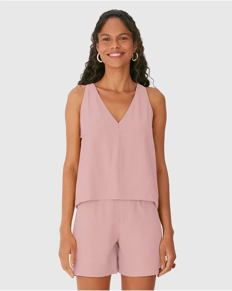 Modelo negra sorridente veste conjunto de shorts e regata alfaiataria rosa bebê da Malwee. 