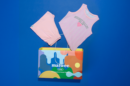 Conjunto da Malwee Kids com a sacola de presente exclusiva da marca em um fundo azul marinho.