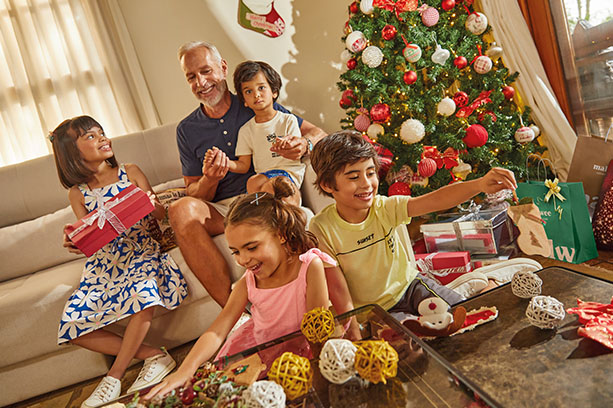 Um homem idoso e quatro crianças vestem peças da malwee e malwee kids enquanto se divertem em uma sala decorada para o Natal.