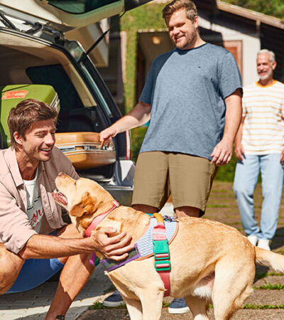 Família de três homens, todos vestindo Malwee, se prepara para viagem junto ao seu cachorro.