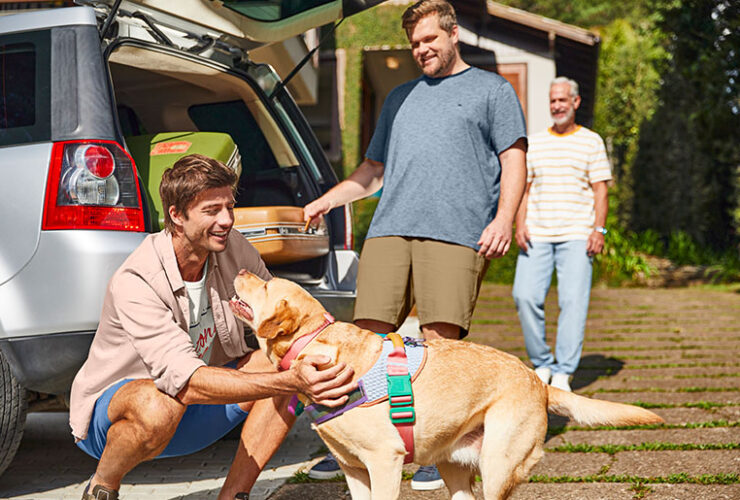 Família de três homens, todos vestindo Malwee, se prepara para viagem junto ao seu cachorro.